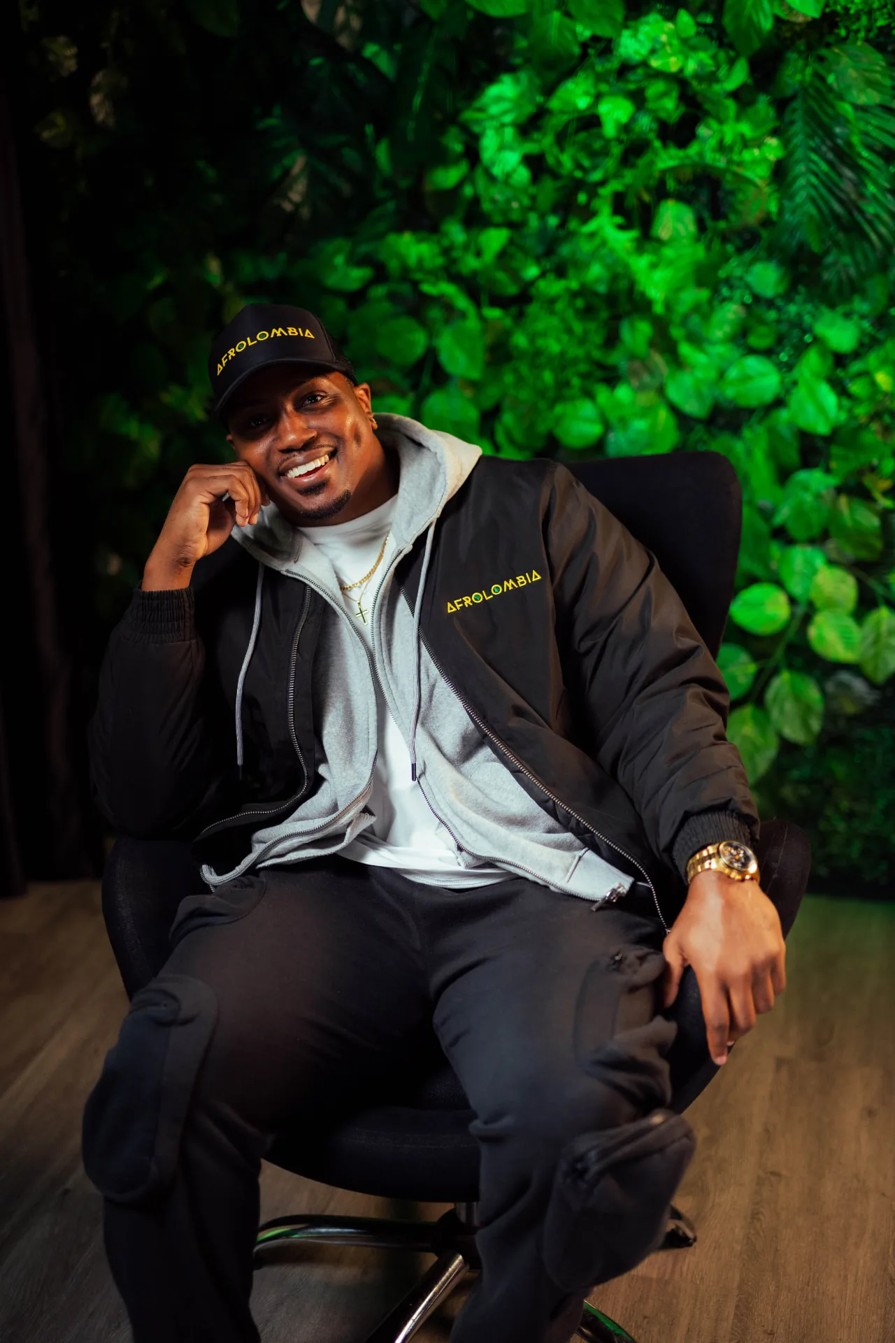 Marcus in full AFROLOMBIA cap and jacket seated in front of a green wall