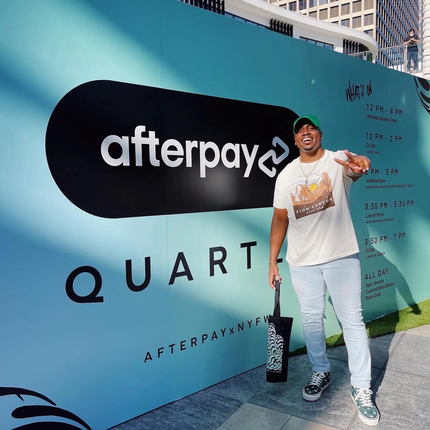 Marcus flashing a peace sign and holding a tote bag in front of the Afterpay x NYFW Quarter event wall